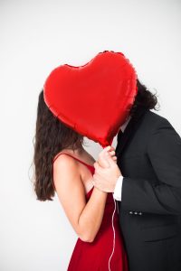 dark haired couple kissing behind love heart balloon