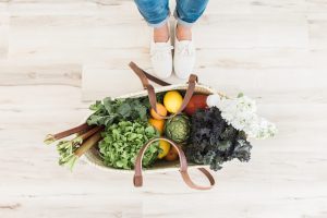 Woman in white shoes standing next to a bag of fruit and vegetables