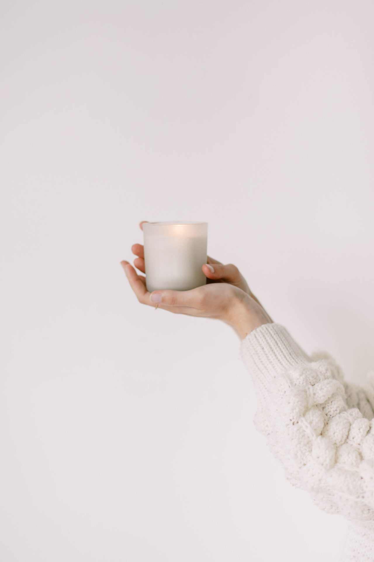 Woman's arms and hands in white sweater holding a white candle