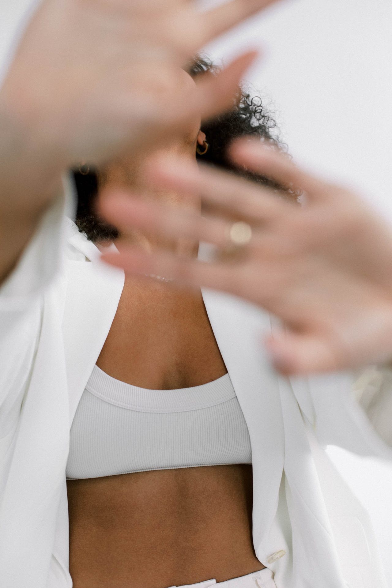 woman wearing white sports bra and shirt holding hands out to camera covering face