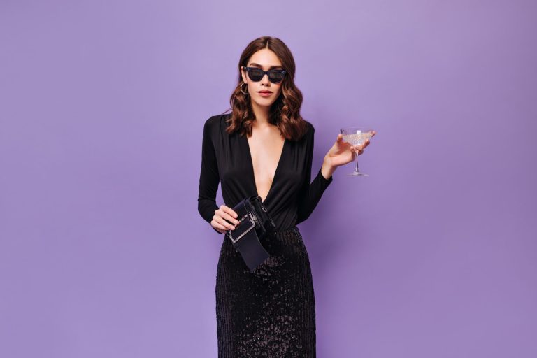 Elegant woman in sunglasses and black dress holds martini glass