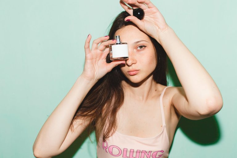 Young woman with long hair posing with perfume bottle in front of face
