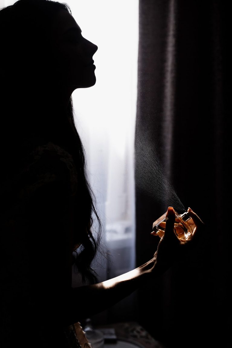Young woman spraying perfume in the dark