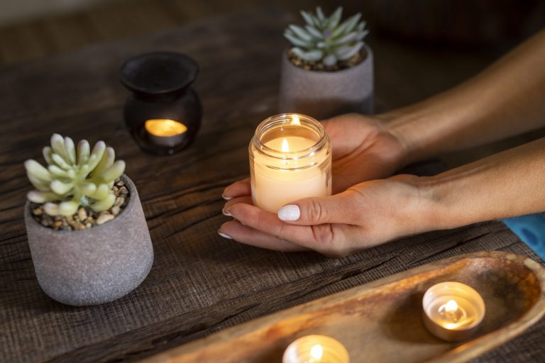 Hand holding a lit candle on a wooden table surrounded by succulents