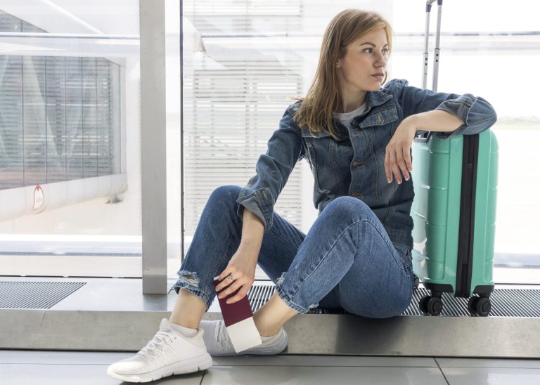 woman in denim jeans waiting at airport with blue suitcase