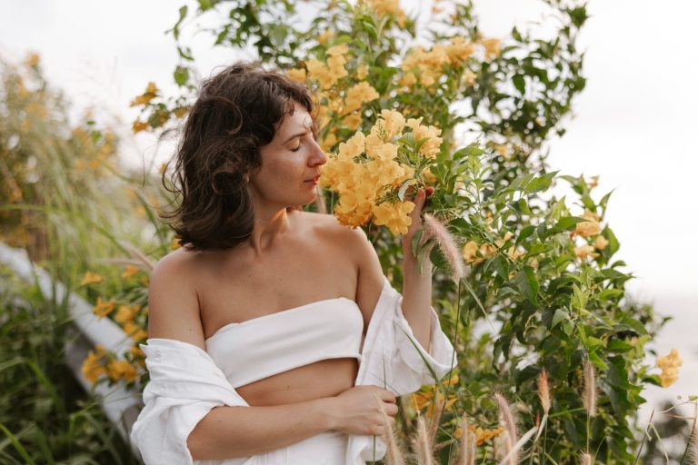 woman wearing white smelling flowers