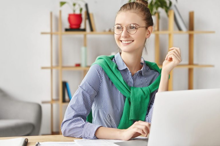 woman in glasses dressed formally sat at a desk with a laptop
