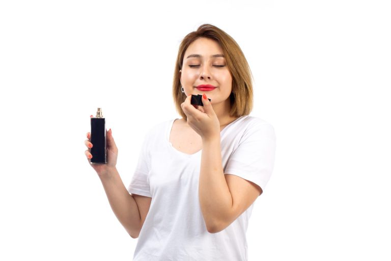 woman wearing white tshirt smelling a bottle of perfume