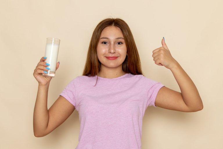 young girl in pink tshirt holding a glass of milk and putting thumb up
