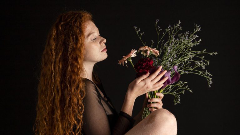 Young woman with ginger hair with bunch of flowers and dark background