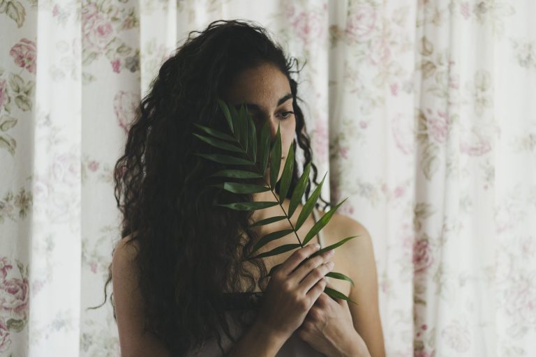 Beautiful woman with black curly hair holding a leaf in front of her face
